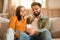 Happy Indian couple on sofa, sharing a joyful moment with smartphone