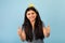 Happy Indian teen girl showing thumbs up gesture with both hands, approving or recommending something, blue background