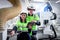 Happy industrial woman and man workers wear helmet and safety vest work together, female check on tablet and point at automatic