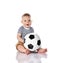 Happy infant baby boy barefooted toddler in t-shirt and pants is sitting holding football soccer ball on white