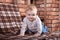 Happy infant baby boy crawling on all fours. Red bricks wall on the background