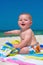Happy infant baby boy sitting on towel at the beach