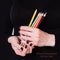 Happy international artists day card. Female hands holding colored pencils on a black background. Manicure with black nail polish