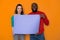 Happy interracial couple holding empty purple banner with copy space in studio