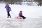 Happy ittle girl pulling her young sister on a sled on the ice in snowy winter park