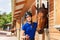 Happy jockey girl with bay horse by riding stables