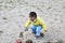 Happy joyful Asia Chinese little boy toddler child play sand on a beach use tools toy shovel buckets and spades outdoor outside