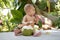 Happy and joyful infant baby at tropical vacation. Eats and drinks green young coconut. Sits on a floor and looking around