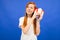 Happy joyful teenager girl with red hair listens to the sounds from the gift box on a blue studio background