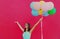 Happy joyful woman with bunch of colorful balloons raising her hands up on a pink background