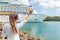 Happy joyful woman waving hello or goodbye hand sign to cruise ship. Caribbean luxury travel vacation concept. Boat leaving harbor