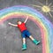 Happy kid boy with rainbow painted with colorful chalks on ground during pandemic coronavirus quarantine. Children