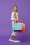Happy kid carry shopping bags on violet background. Little shopaholic smile with paper bags. Girl shopper smiling with