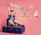 Happy kid dreams and wish to travel. Funny child boy with dream figure sitting on the suitcase. Travel and adventure
