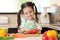 Happy kid girl chopping tomatoes on cutting board with knife in kitchen