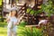 happy kid girl in hat playing little gardener and helps to water flowers