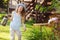 Happy kid girl in hat playing little gardener and helps to water flowers