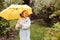 Happy kid girl in warm knitted sweater playing and hiding under umbrella on the walk in rainy autumn day in park