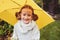 Happy kid girl in warm knitted sweater playing and hiding under umbrella on the walk in rainy autumn day in park