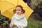 Happy kid girl in warm knitted sweater playing and hiding under umbrella on the walk in rainy autumn day in park