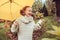 Happy kid girl in warm knitted sweater playing and hiding under umbrella on the walk in rainy autumn day in park