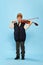 Happy kid, little musician wearing big size clothes posing with violin isolated over blue background. Education, music