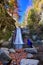 Happy kid near photo camera on tripod with a waterfall in background in autumn