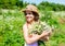 Happy kid smile in sun hat with chamomile flower bunch on sunny landscape vacation in countryside summertime, summer