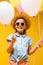 happy kid in straw hat and sunglasses holding balloons and pointing with finger isolated on yellow.