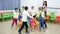 Happy kids and female teacher playing musical chairs together during break in classroom at elementary sch