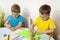 Happy kids with yellow and blue shirts doing arts and crafts together at their desk. Children draw on colored paper