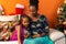 Happy Latin Afro-descendant Colombian mother and daughter sitting on the sofa next to the Christmas tree checking the cell phone