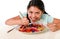 Happy Latin female child eating dish full of candy and gummies with fork and knife and big cola bottle in sugar abuse