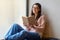 Happy latin lady in glasses reading favorite book, sitting near window in cafe during daytime, after quarantine time