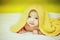 Happy laughing baby wearing yellow hooded towel lies on parents bed after bath or shower . newborn holds its head. Beautiful baby