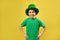 Happy laughing boy wearing leprechaun green hat poses to the camera on a yellow background. Saint Patrick`s Day. Copy space