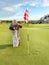 Happy laughing senior woman plays golf on golf course in evening attire. Ball is near hole with flag