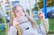 Happy laughing teen girl with long hair wearing a knitted cardigan enjoying a swing ride on a sunny autumn playground in