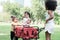 Happy little African American and Caucasian kids girls playing together at park in summer. Children towing pushing red trolley car