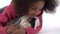 Happy little african curly girl is stroking fluffy Sheltie guinea pig at white background. Close up. Slow motion