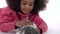 Happy little african curly girl is stroking fluffy Sheltie guinea pig at white background. Close up. Slow motion