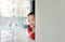 Happy little Asian baby boy hide behind a corner room. Small children playing peekaboo game indoor