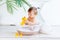 Happy little baby girl washes in a basin with foam and water in a bright room at home and plays with a yellow rubber duck