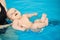 Happy little baby swimming in water pool with help from mothers hands