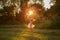 Happy little blonde girl in gray dress dancing in park, sunlight, sunset.