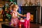 Happy little blonde girl playing near Christmas tree with toy kitchen. Xmas morning in decorated living room with fireplace and