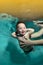 A happy little boy with Down syndrome in the arms of a parent underwater in a turquoise water pool. The child looks into