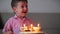 Happy little boy of four sits on the couch looking at the burning candles on the birthday cake, makes a birthday wish