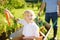 Happy little boy having fun in a wheelbarrow pushing by dad in domestic garden on warm sunny day