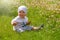 Happy little boy sits in a field of green grass and flowers